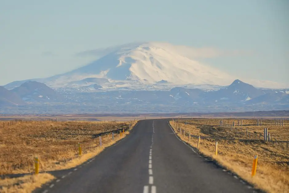 Carretera recta atraviesa llanura árida hacia volcán nevado bajo cielo azul claro
