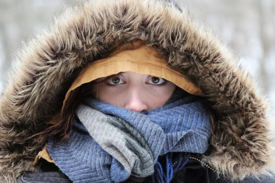 Persona abrigada con capucha de piel y bufanda azul en tormenta de nieve